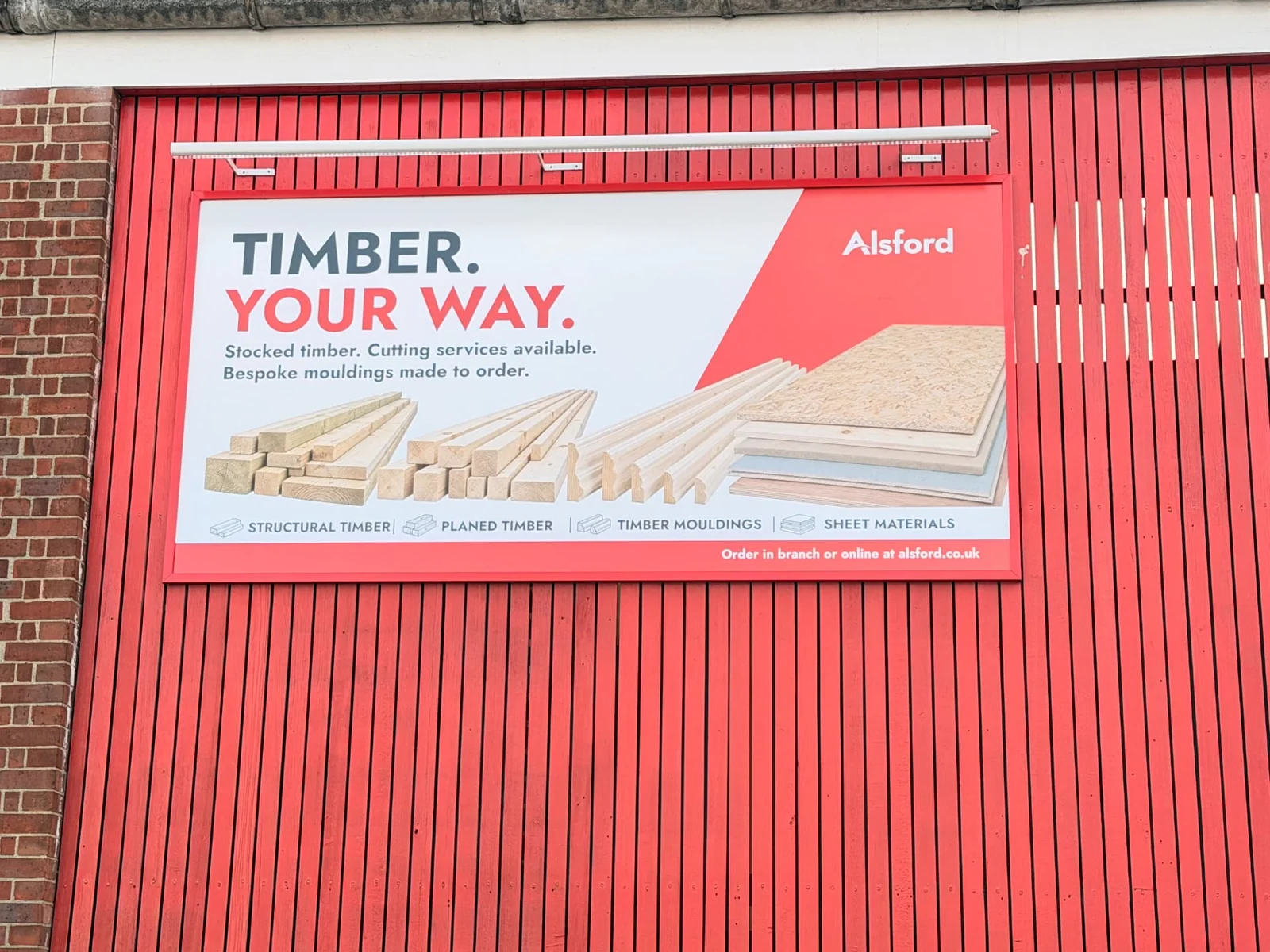 Printed Alsford billboard advertising timber, mounted on a red clad wall